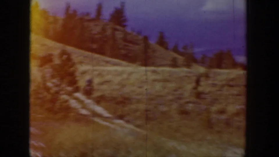 Soft 8mm frame from the Wyoming sequence showing a distant horse rider on a winding hillside path.