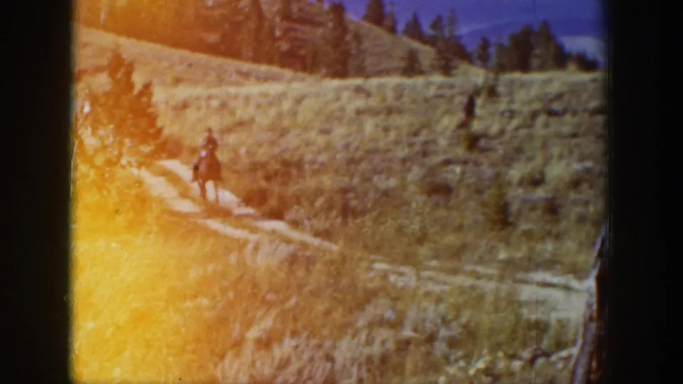 1939 Wyoming home-movie frame showing a rider on a winding hillside trail with warm light leak at the frame edge.