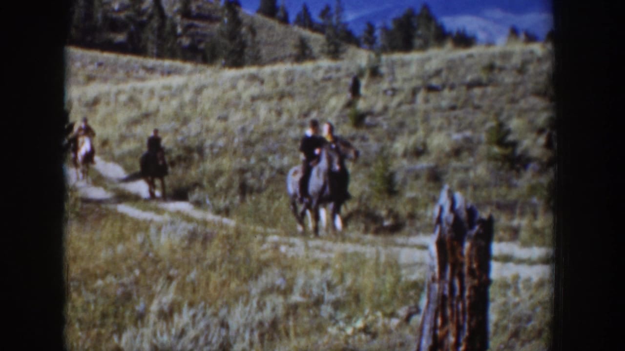 1939 Wyoming home-movie frame showing three men riding horses through a grassy valley, with a weathered wooden post in the foreground.