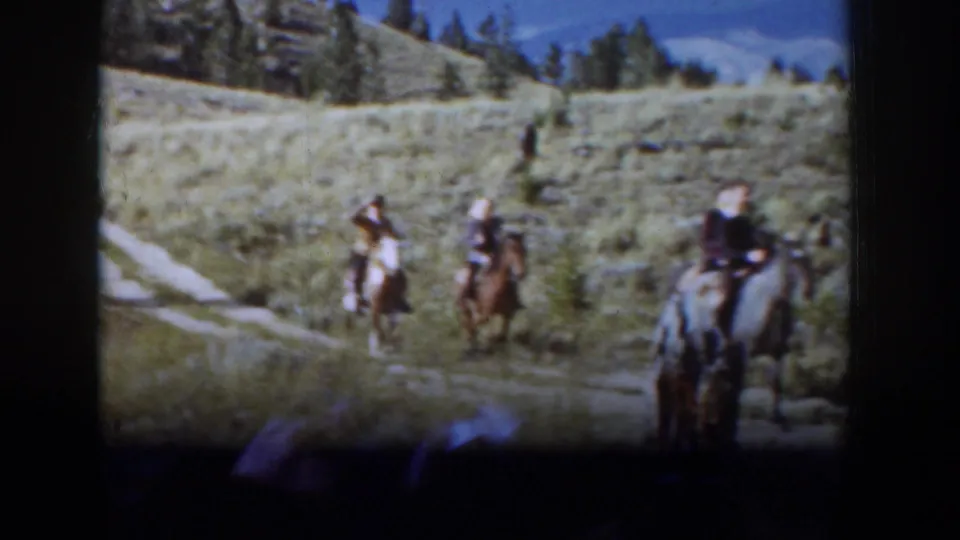 1939 Wyoming home-movie still with three men on horseback crossing a valley path under blue sky and scattered trees.