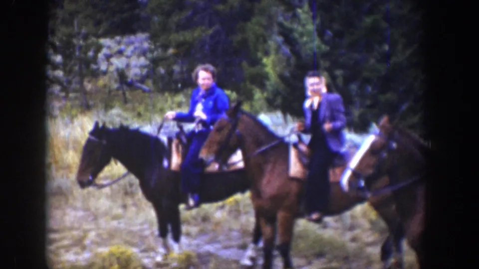 1939 Wyoming frame with two adult riders on saddled horses in a grassy, wooded area.