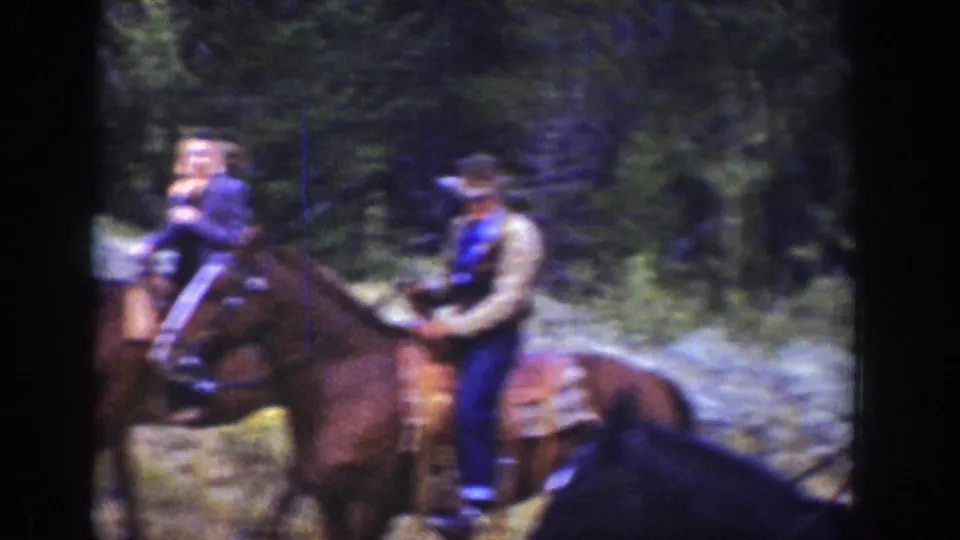 1939 Wyoming home-movie frame showing mounted riders near trees and a rocky hillside.