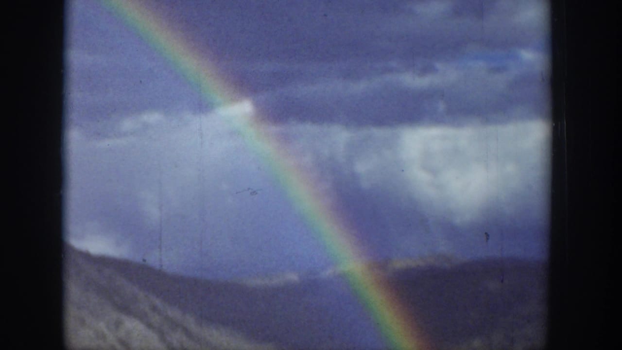 1939 Wyoming 8mm frame showing a bright rainbow against stormy sky above rolling hills.