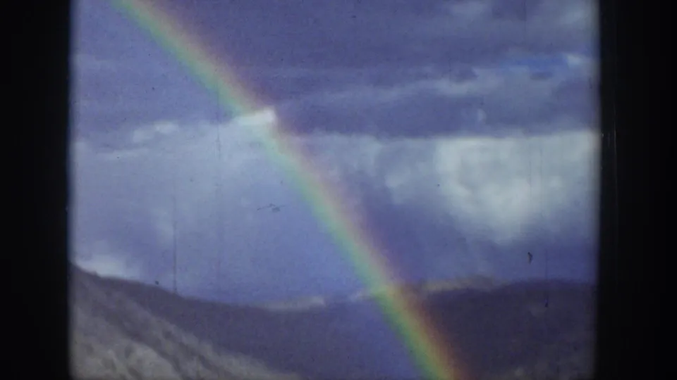 1939 Wyoming 8mm frame showing a bright rainbow against stormy sky above rolling hills.