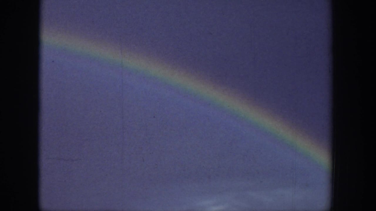 Rainbow band crossing a purple-blue sky above a faint low horizon.