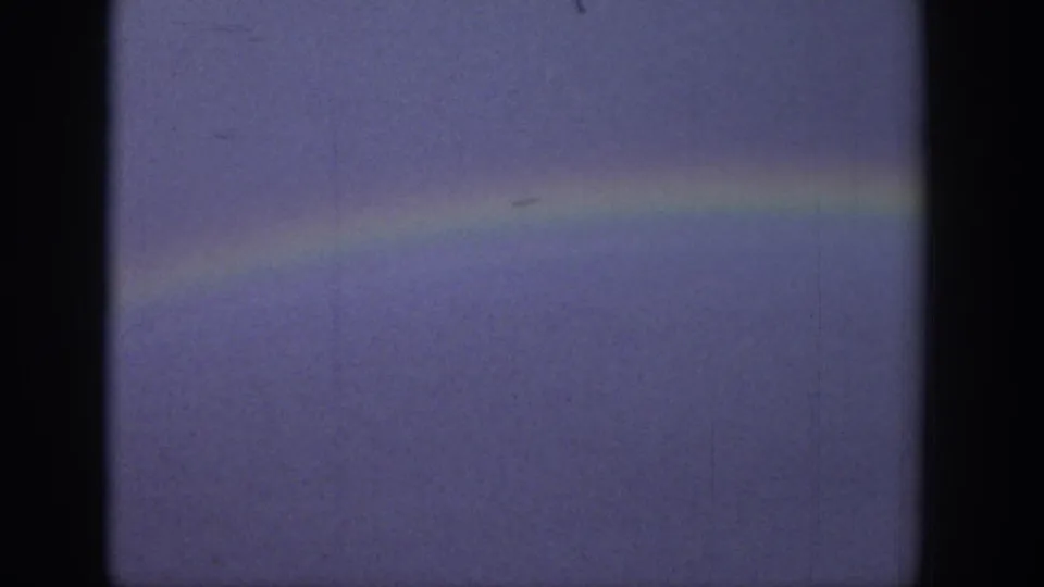 1939 Wyoming 8mm frame showing a muted rainbow band across a pale, grainy sky.