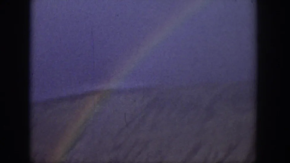 1939 Wyoming 8mm frame showing a rainbow near a sloping ridge beneath a storm-tinted sky.