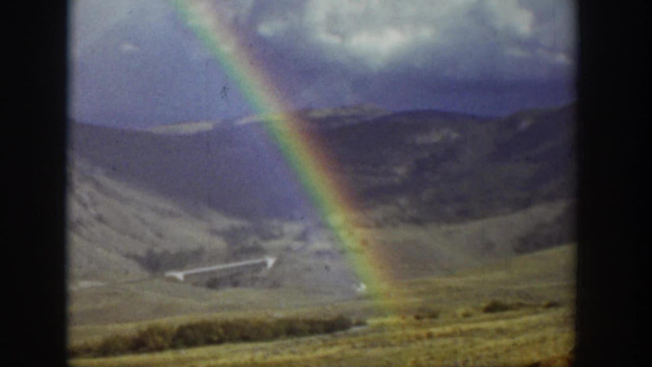 Bright rainbow over hills and a wide valley landscape.