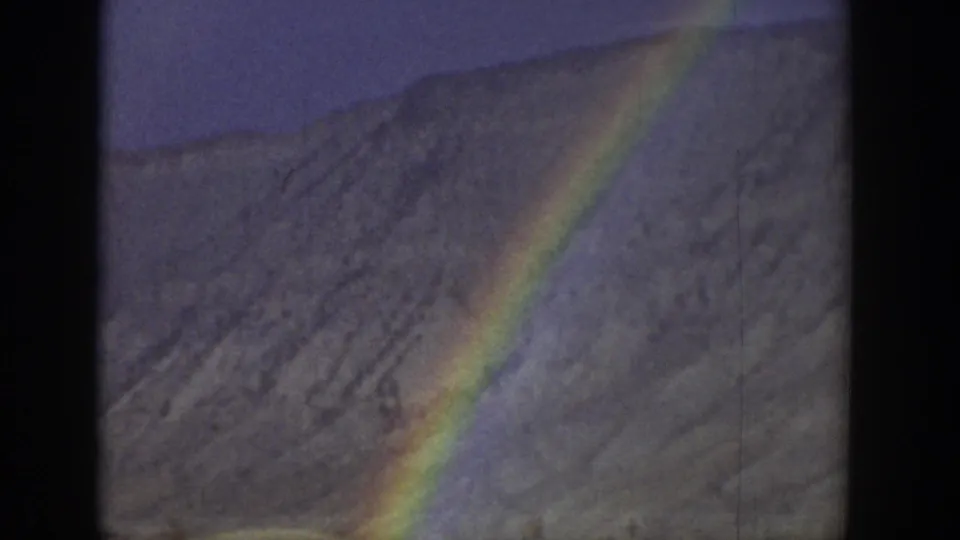 1939 Wyoming 8mm frame showing a rainbow band cutting across a softly focused mountain slope and muted valley foreground.