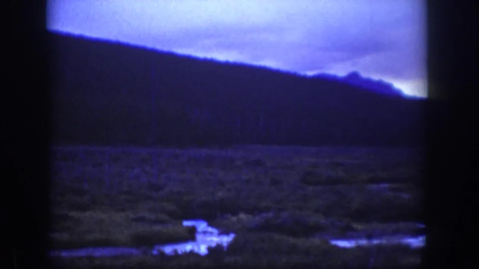 1939 Wyoming 8mm frame looking across a dark hill and open meadow, with a pale reflective stream or track in the foreground.