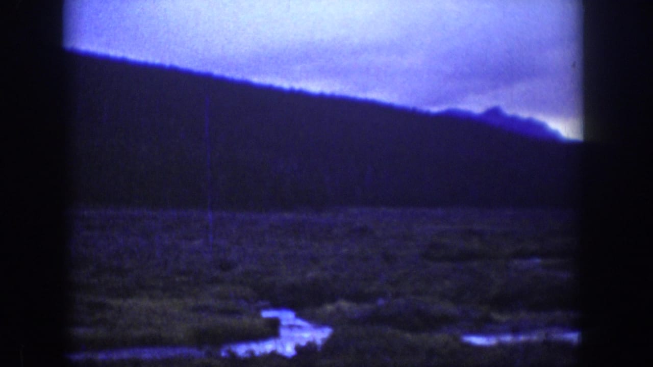 Dark wooded hills under a cloudy blue-purple sky with reflective lowland water below.