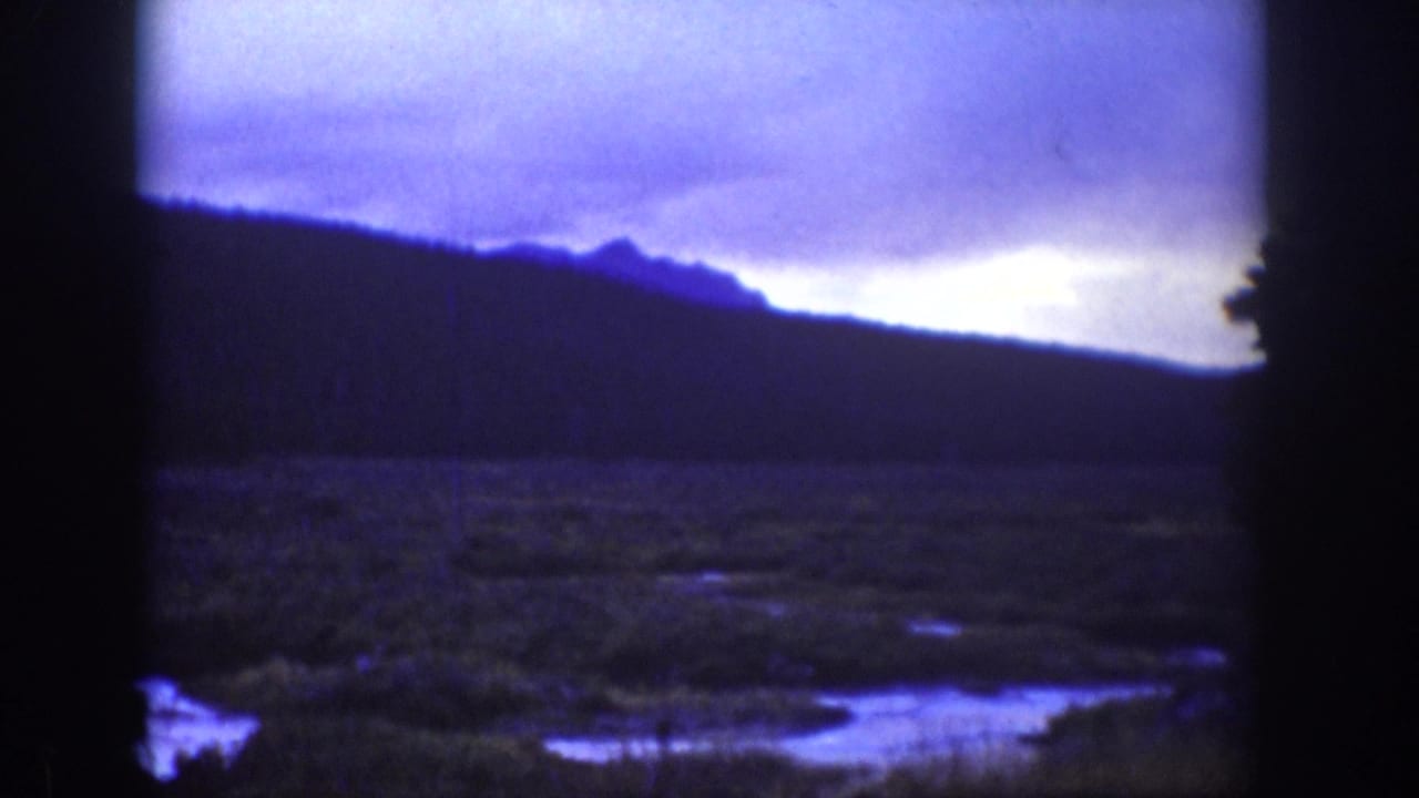 Similar dark hillside landscape seen through film borders with pale cloudy sky and lowland water.