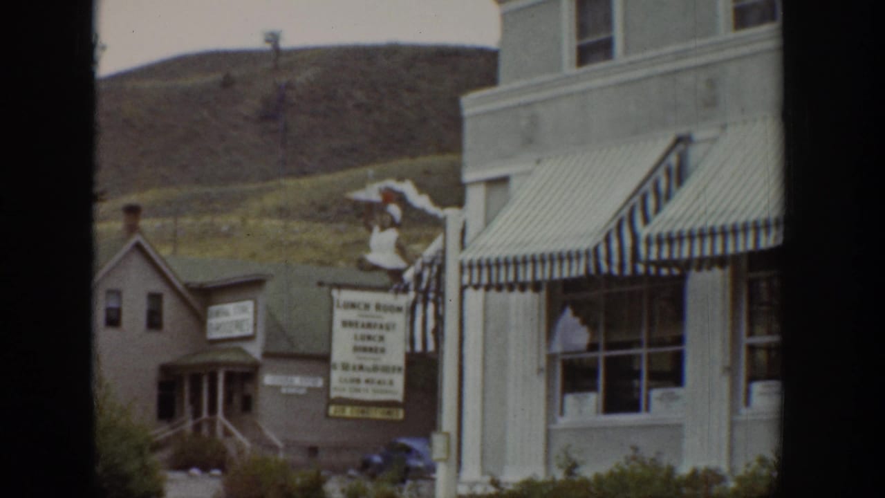 1939 Wyoming street view with striped awnings, a visible lunch room sign, neighboring building, and hillside behind the storefronts.