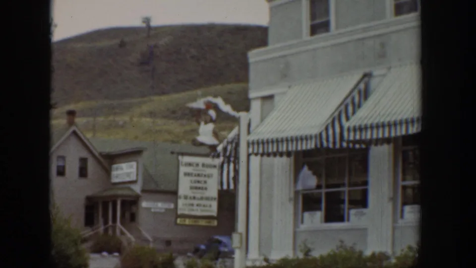 1939 Wyoming street view with striped awnings, a visible lunch room sign, neighboring building, and hillside behind the storefronts.