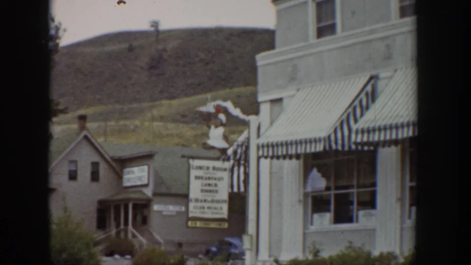 1939 Wyoming home-movie frame centered on a storefront with striped awnings, lunch room signage, windows, and adjacent small building.