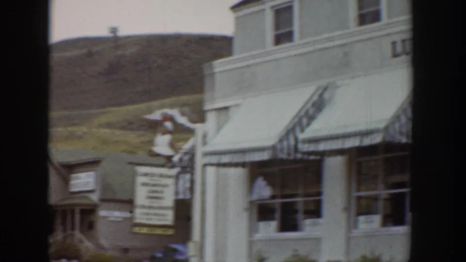 1939 Wyoming street frame showing a storefront facade with striped awnings, windows, signage, and open hillside above the town.