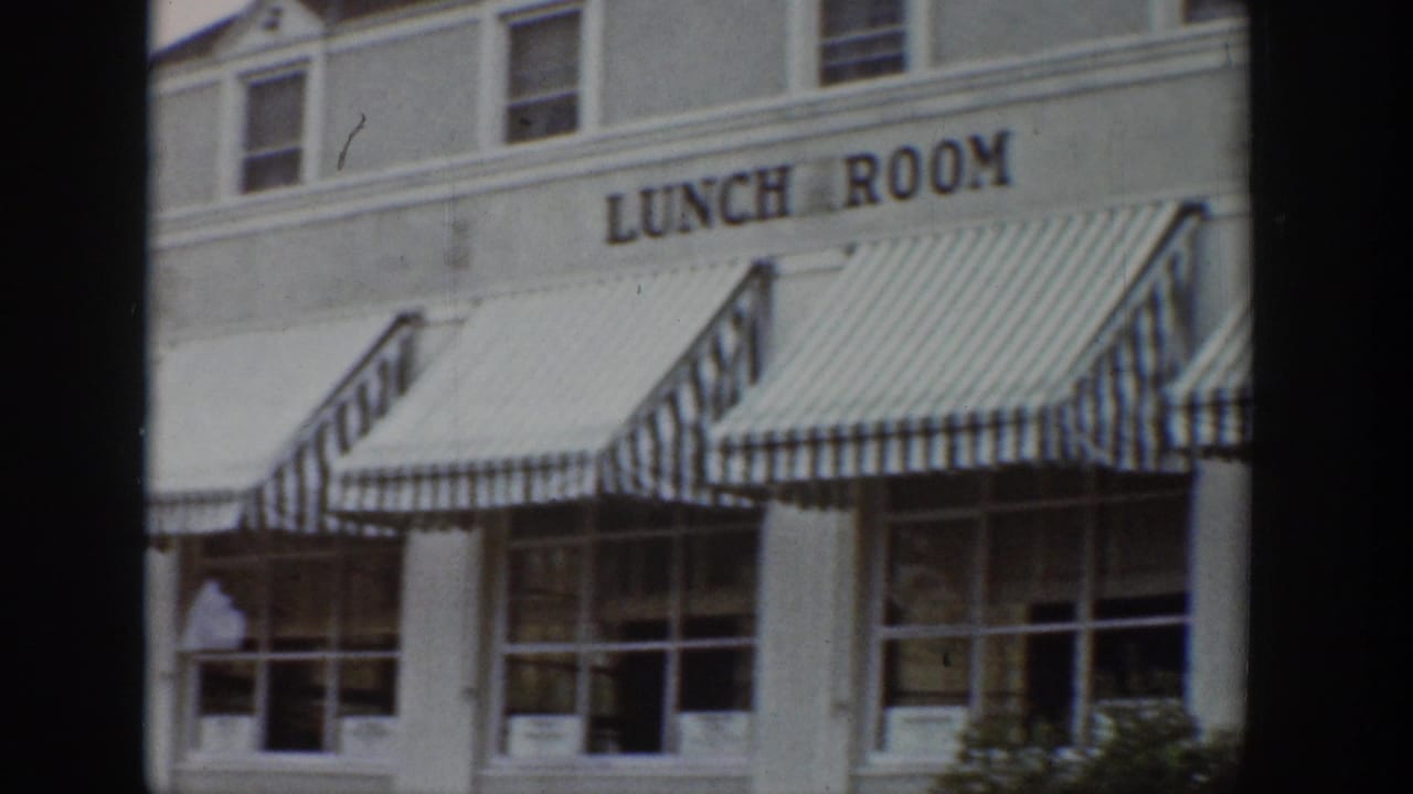 1939 Wyoming 8mm frame showing a white lunch room facade with striped awnings, windows, and partial storefront detail.