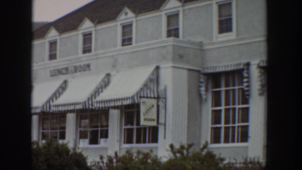 1939 Wyoming 8mm frame showing the lunch room corner, striped awnings, upper dormer windows, and a hanging sign.
