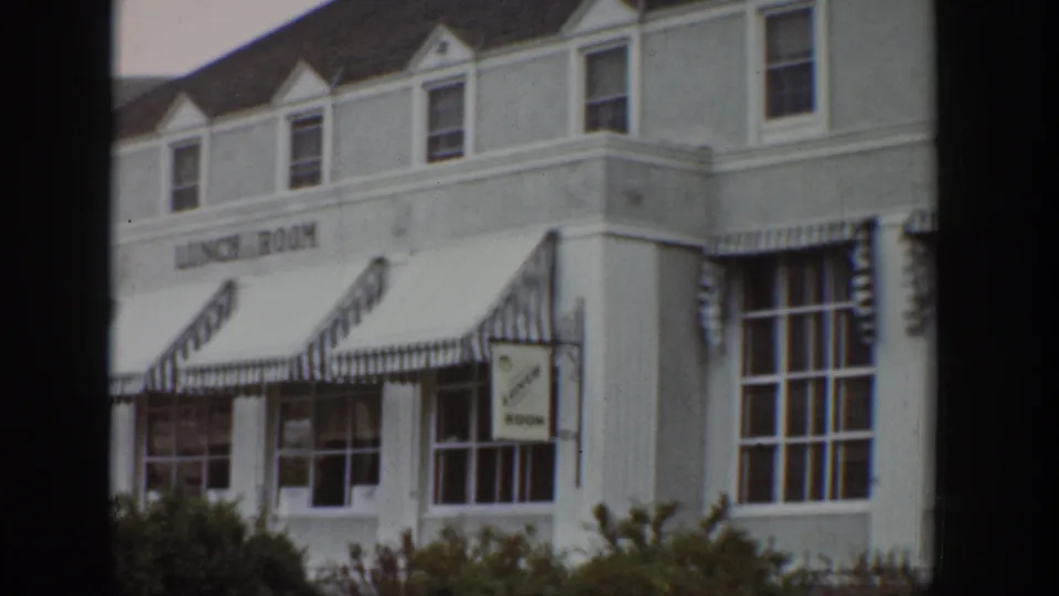 1939 Wyoming 8mm frame showing the lunch room corner, striped awnings, upper dormer windows, and a hanging sign.