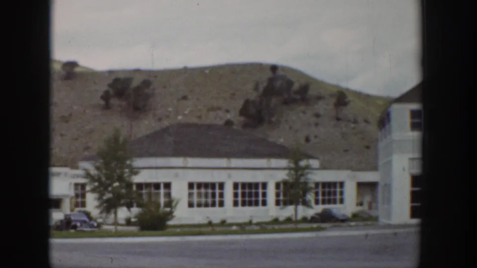 1939 Wyoming 8mm frame showing a white resort building, road frontage, small car, trees, and rocky hillside behind it.