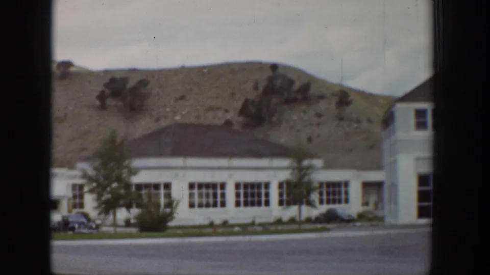 1939 Wyoming 8mm frame showing the resort exterior from across the road, with hillside terrain and a rounded roof section.