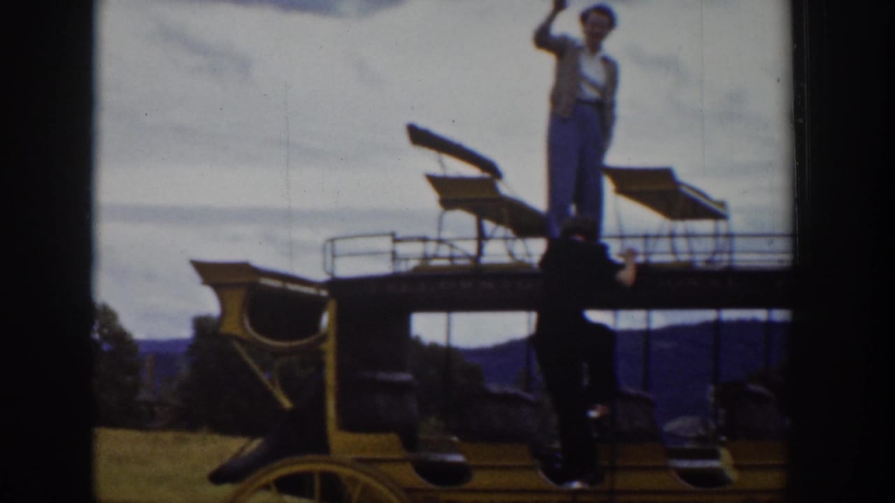 In 1939 Wyoming footage, a woman stands on the roof platform of a yellow stagecoach-style vehicle while a man reaches up to assist her.
