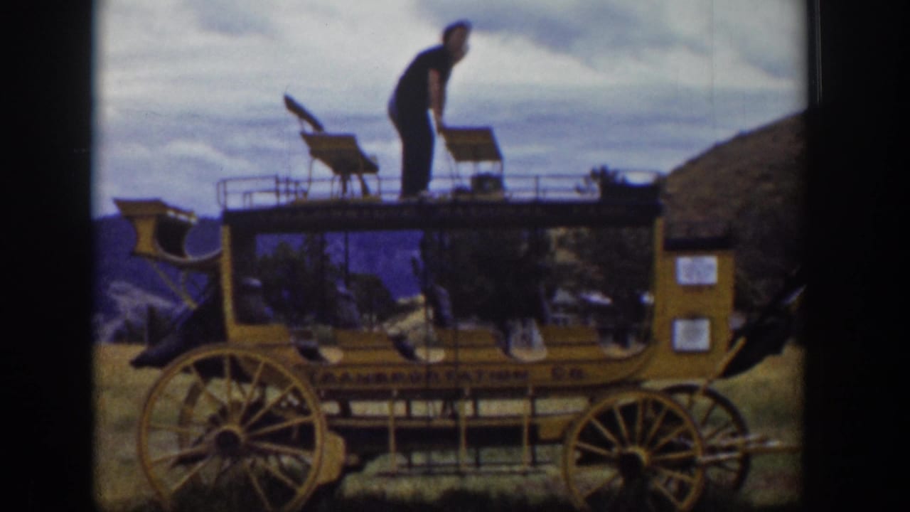 Man stands on the roof platform of a yellow stagecoach-style vehicle.