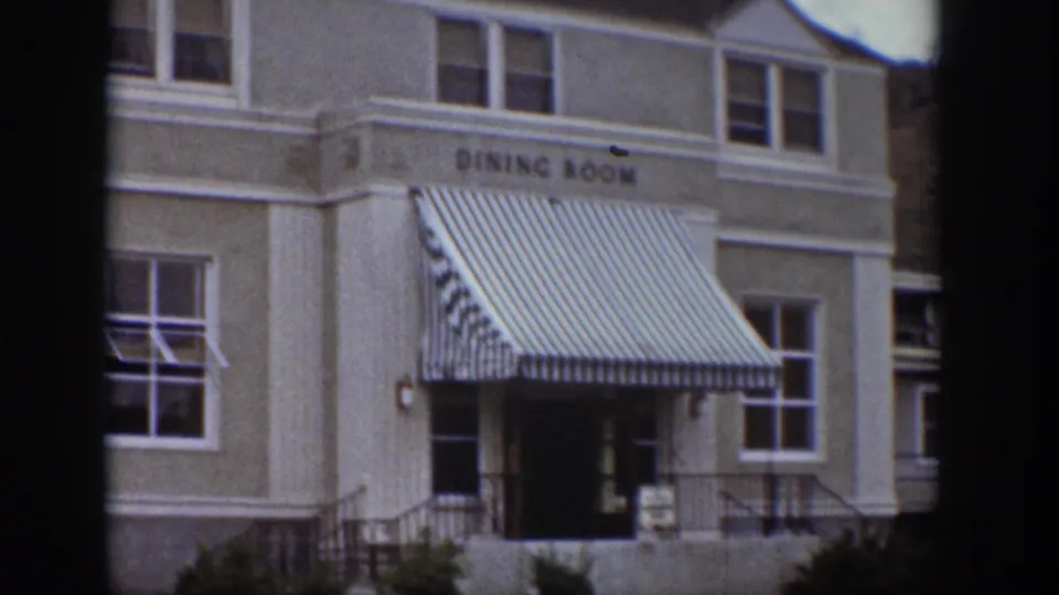 Exterior of a dining-room building in the Wyoming clip, showing striped awnings, windows, railings, and an entrance.