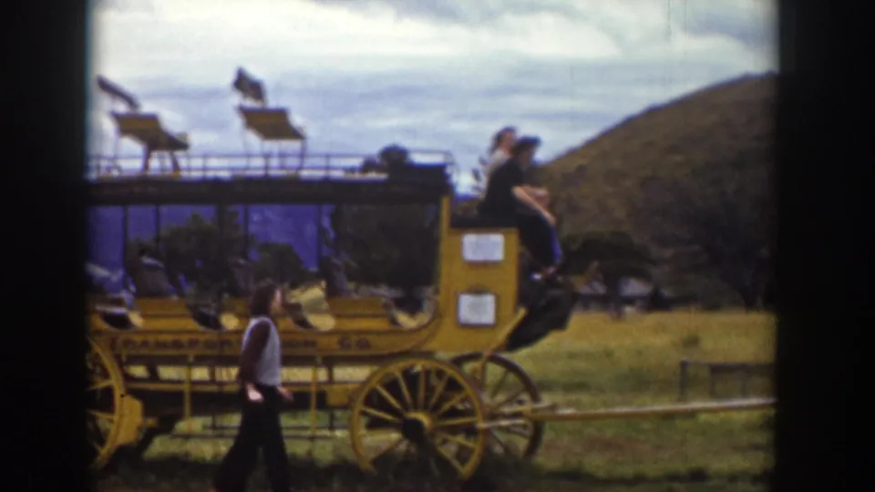 1939 Wyoming 8mm frame of the yellow stagecoach with one person seated near the front and another walking beside it.