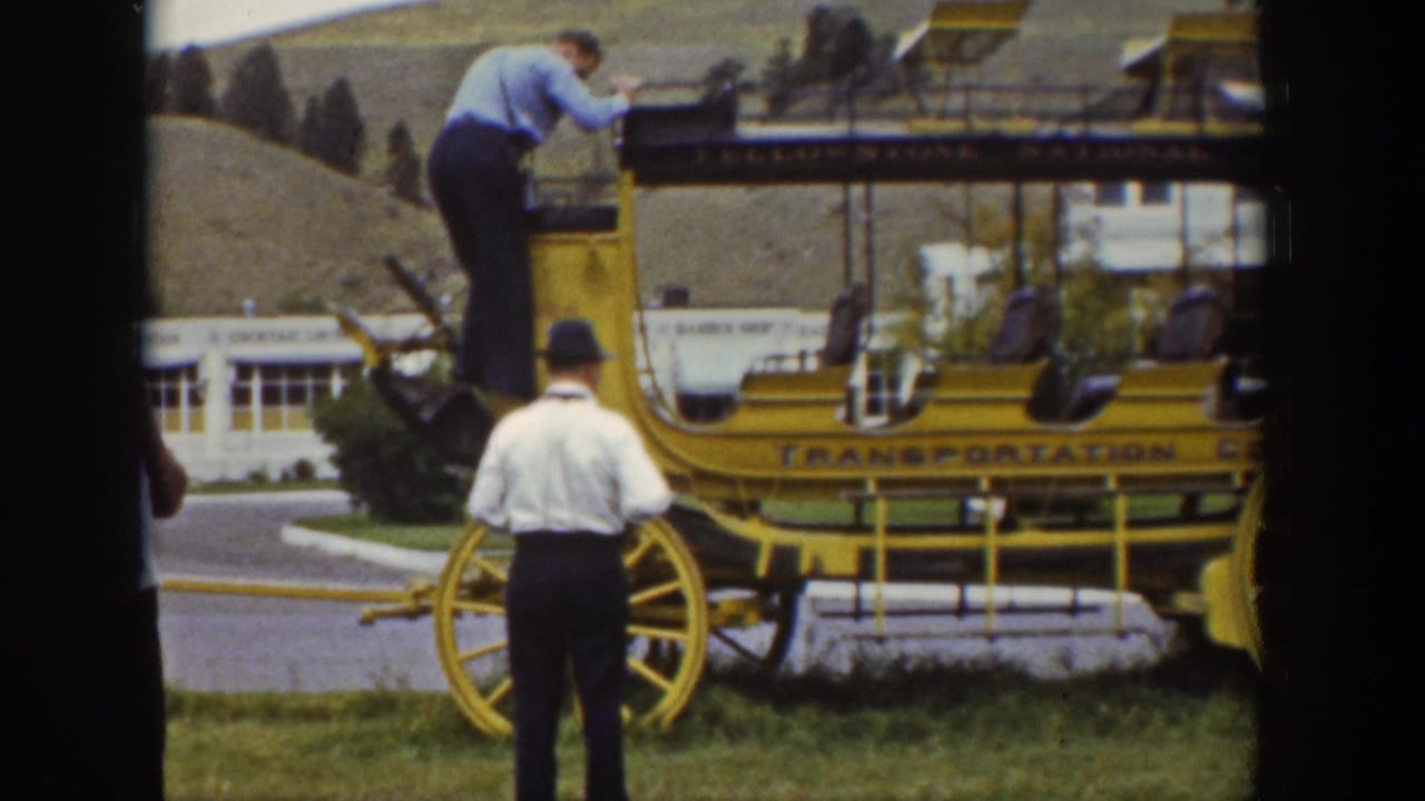 1939 Wyoming home-movie frame showing men around a bright yellow wagon marked for Yellowstone transportation, with a building and hillside behind.