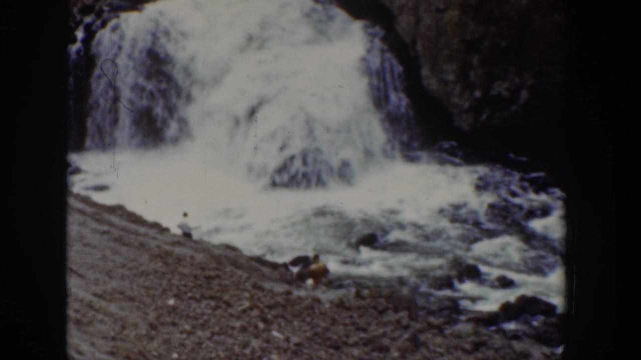 1939 Wyoming 8mm frame of a waterfall dropping into foaming water beside a sloped gravel riverbank.