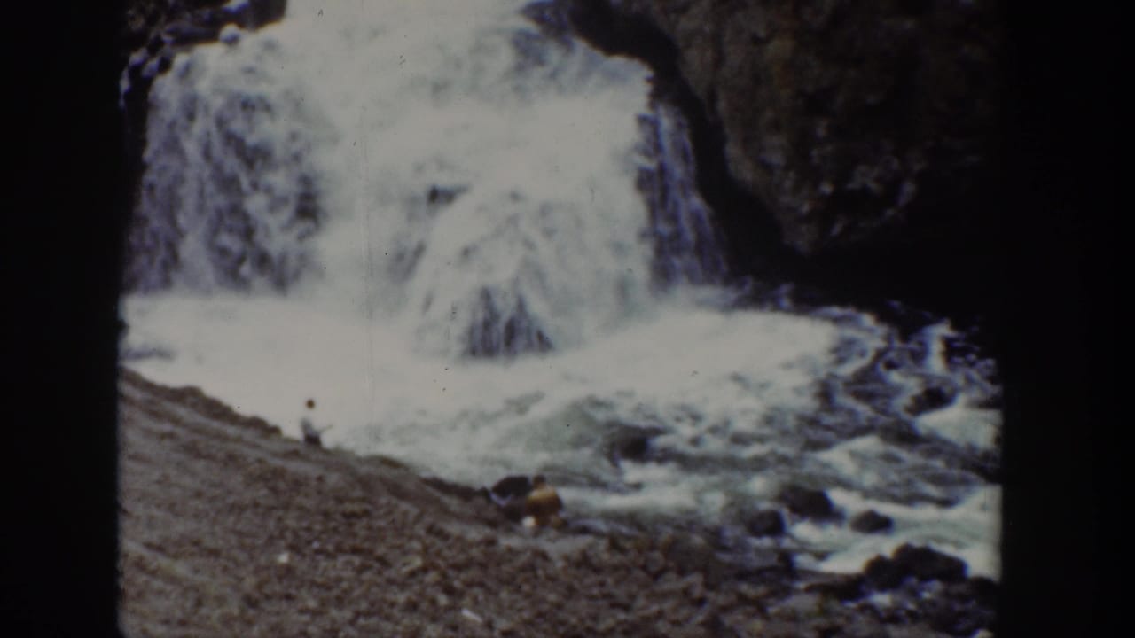 1939 Wyoming 8mm frame showing a waterfall and fast water with a distant person near the rocky bank.
