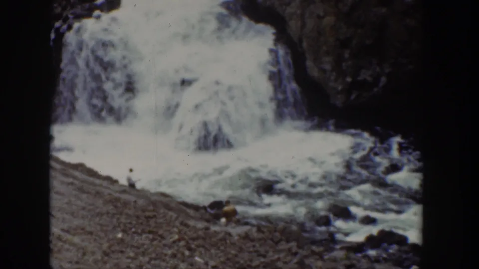1939 Wyoming 8mm frame showing a waterfall and fast water with a distant person near the rocky bank.