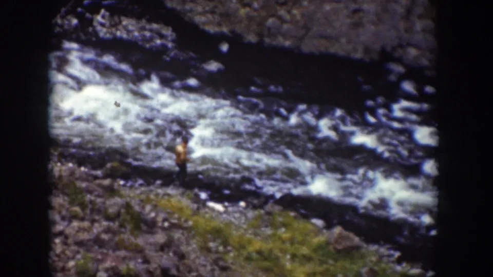 1939 Wyoming 8mm frame of a visitor on a rocky bank watching whitewater below the falls.