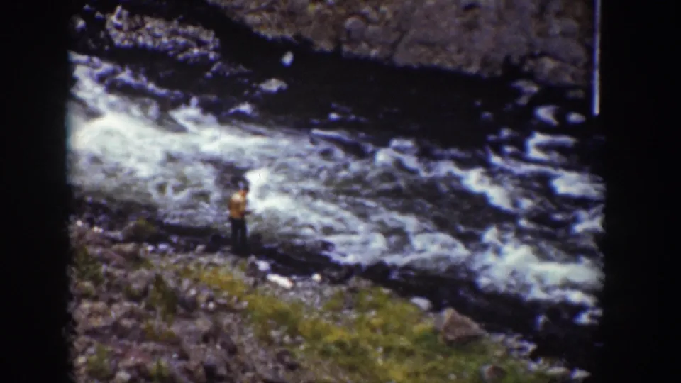 1939 Wyoming 8mm frame with a person in period outdoor clothing near fast whitewater and rocks.
