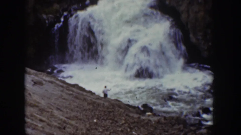 1939 Wyoming 8mm frame showing a large waterfall and a distant man on the rocky bank below.