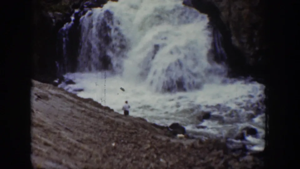 1939 Wyoming 8mm frame showing a distant person near a powerful waterfall and foaming riverbank.