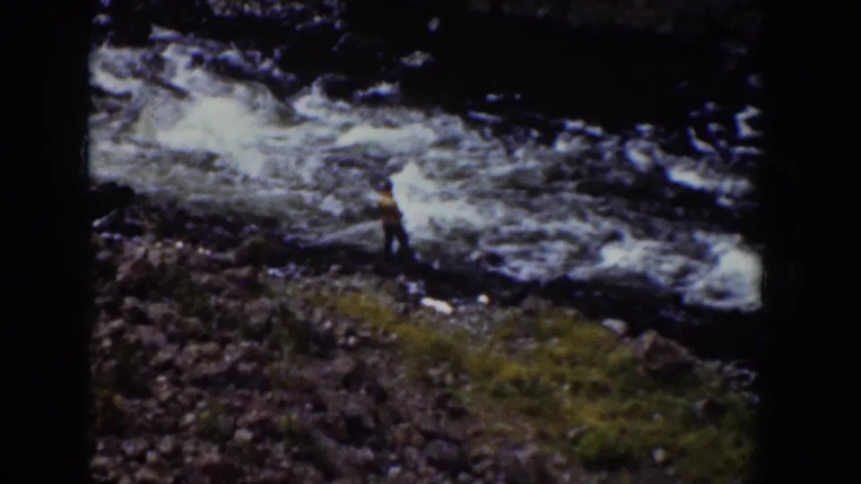 1939 Wyoming 8mm frame with a person in a yellow top on a rocky riverbank beside whitewater.