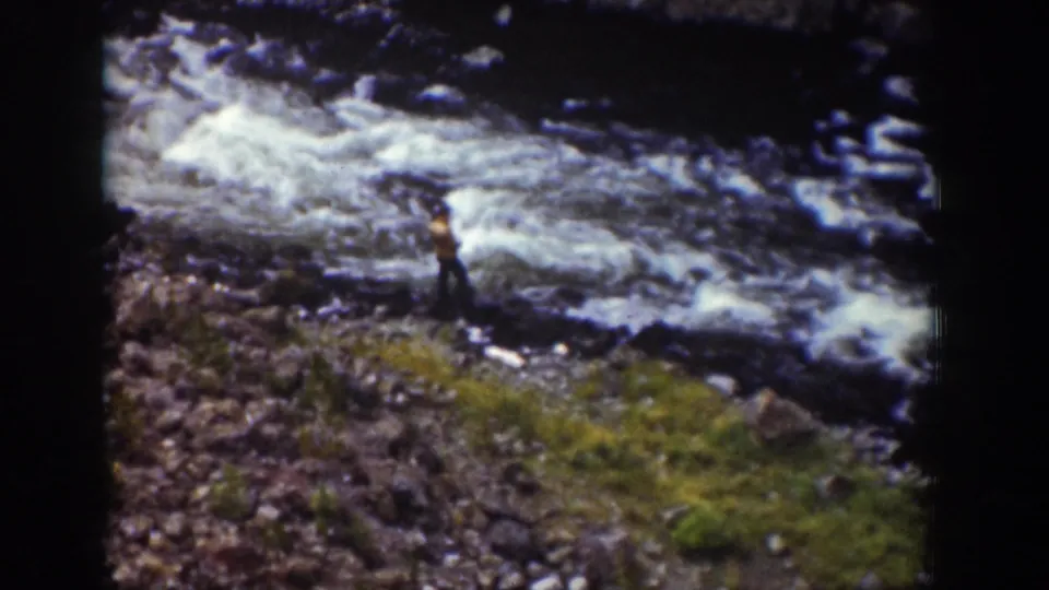 1939 Wyoming 8mm frame showing a person beside a rushing river, with rocks and grass in the foreground.