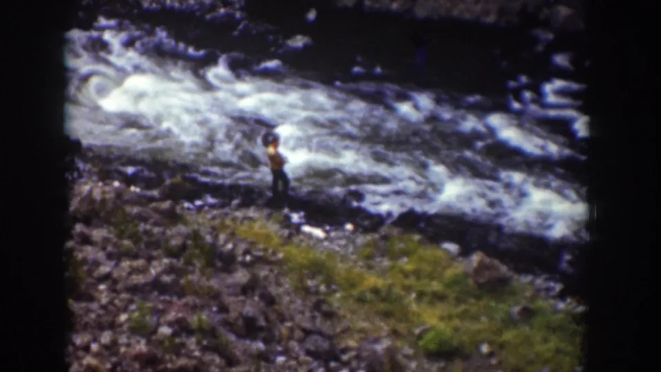 1939 Wyoming 8mm frame with a distant person on the riverbank beside rushing whitewater and a grassy patch.