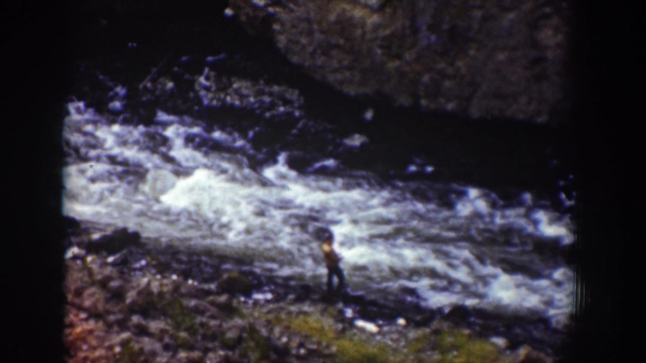 1939 Wyoming 8mm frame with a distant figure on the riverbank beside foaming rapids and dark rocks.