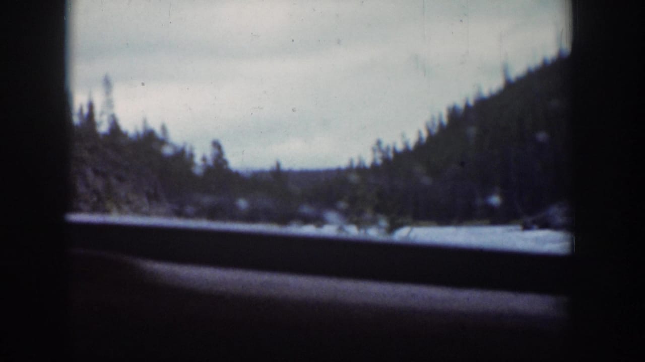 1939 Wyoming home-movie frame showing a snowy river bend, forested hills, and overcast sky through a car window.
