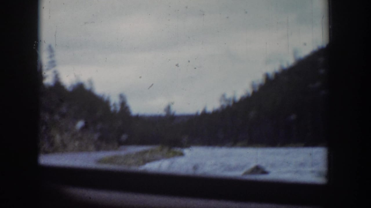 River, snow patches, and wooded hills viewed through a vehicle window.