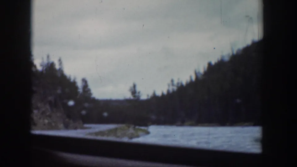 A 1939 Wyoming travel view shows a snowy stream, evergreen slope, and cloudy sky from inside a moving car.