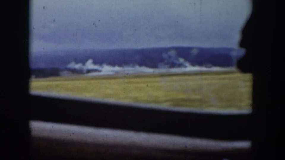 The clip shifts to a grassy Wyoming field with distant mountains, still framed by the car window and 8mm film texture.