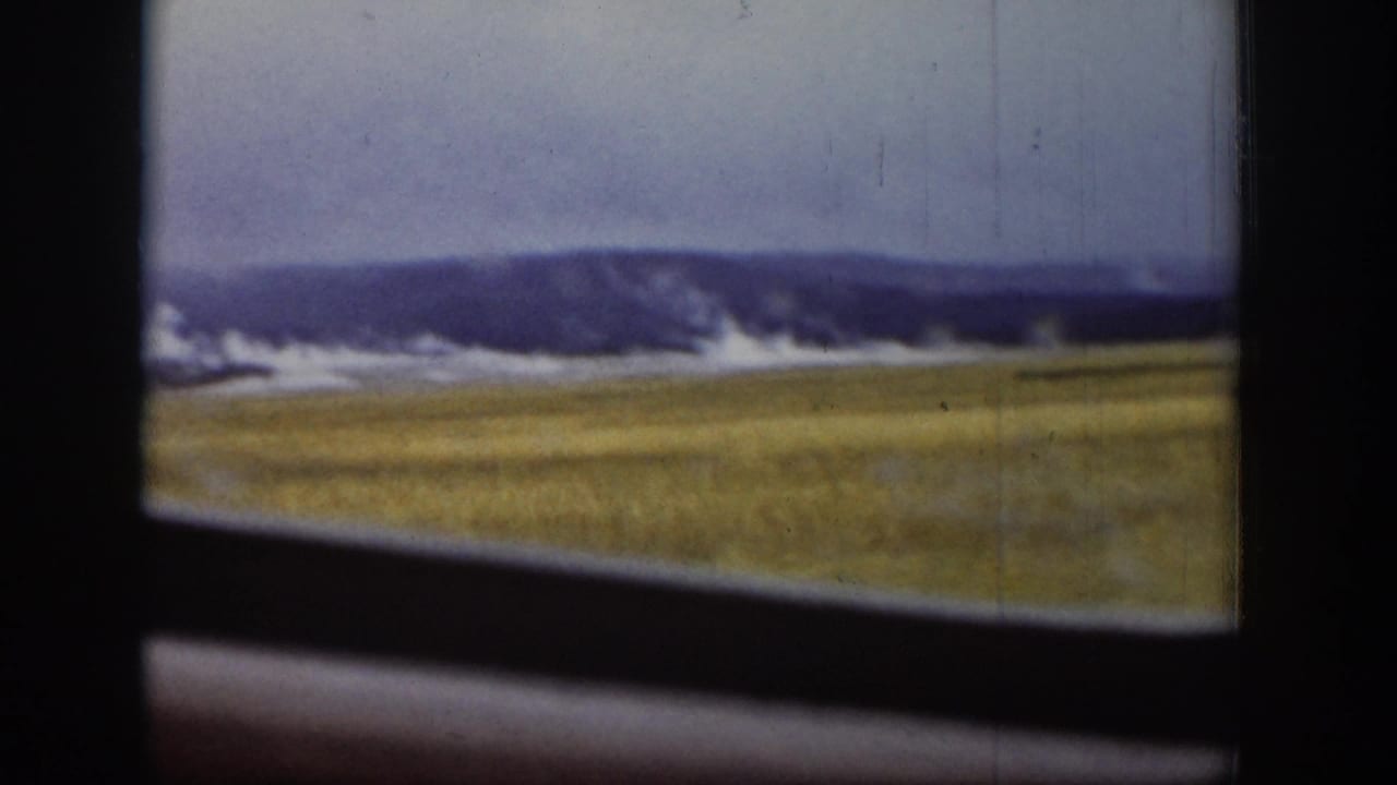 1939 Yellowstone home-movie frame showing Old Faithful erupting in the distance through a moving vehicle window.