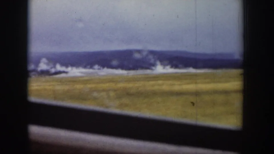 Vehicle-window view of the Old Faithful area in Yellowstone, with steam rising beyond an open field in 1939 footage.