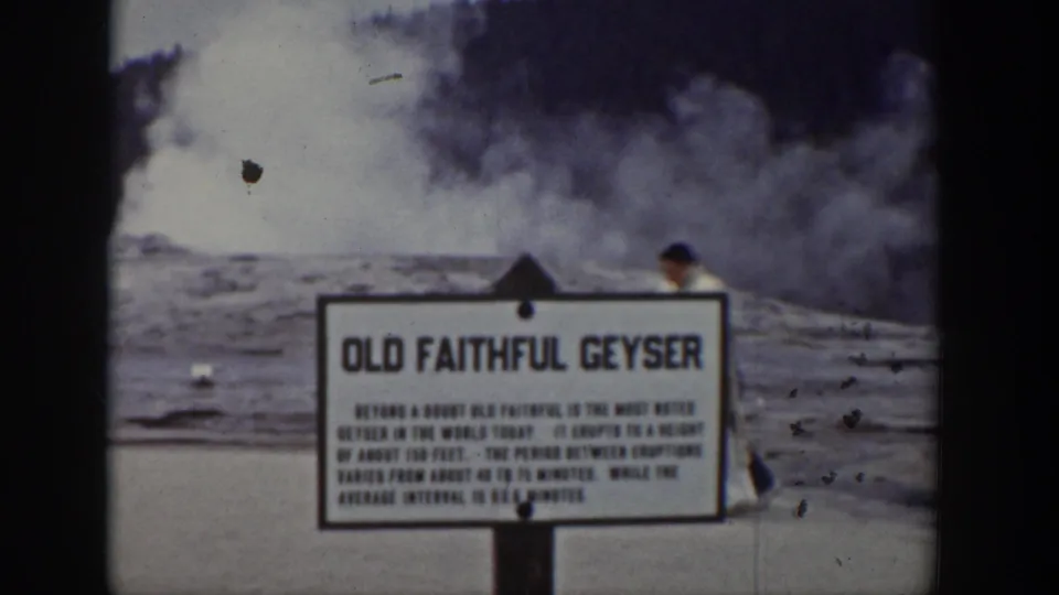 Final 1939 Wyoming frame showing the Old Faithful sign, eruption steam, and a partially visible adult at the right.