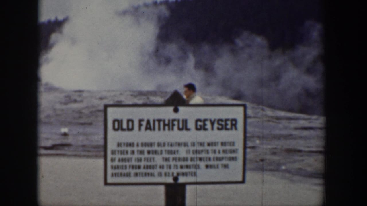 1939 Yellowstone home-movie frame showing the Old Faithful Geyser sign, steam in the background, and a visitor partly visible nearby.