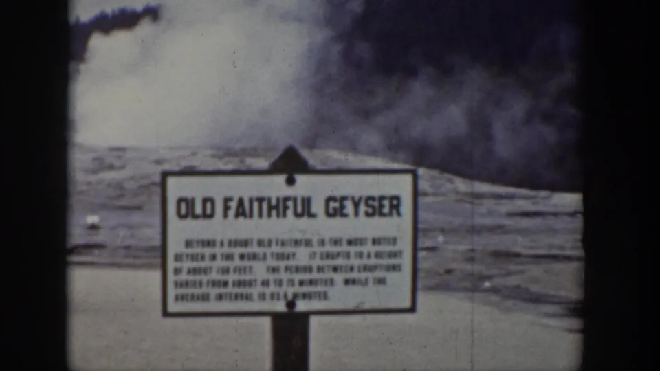 1939 Yellowstone frame showing the Old Faithful Geyser sign in the foreground with dense steam rising behind it.